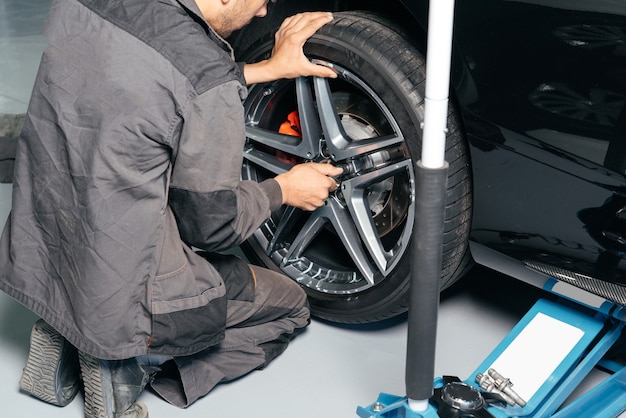 Mechanic repairing car wheel in auto repair shop using lift jack and electric drill to loosen the