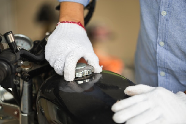 Mechanic repairing motorcycle in workshop garage Man fixing motorbike in repair shop Man opening motorcycle fuel tank cap Repairing and maintenance concepts