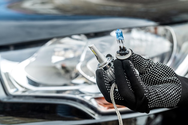 The mechanic's hands hold two diferent car bulbs for replacement in car