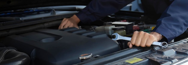 Mechanic's hands and mechanic wrench are working on the engine of a car.