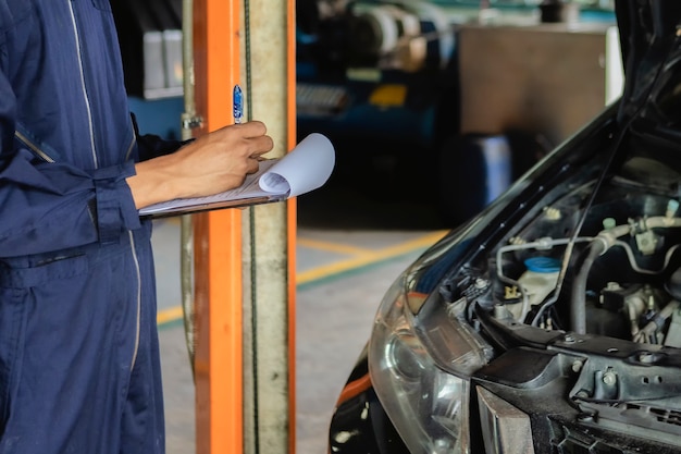 A mechanic service car in garage is check a list cars.