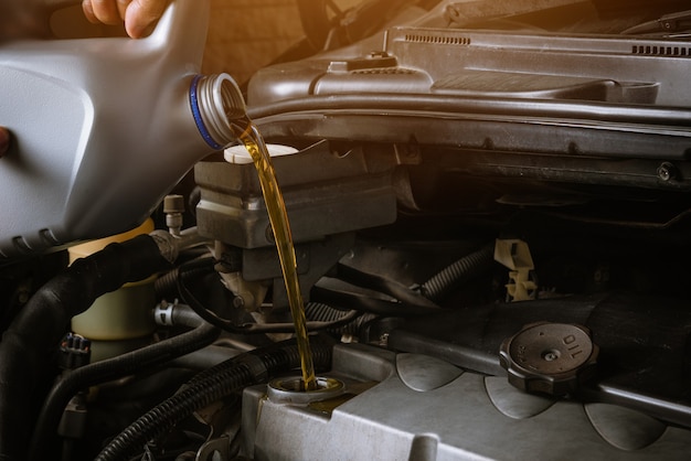 Mechanic in service to repair the car, refueling and pouring from bottle to change lubricant