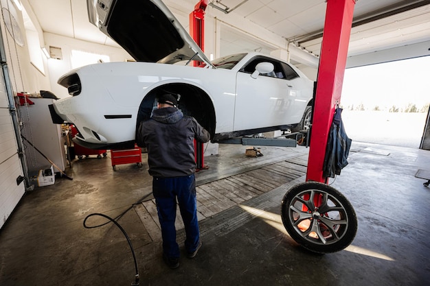 Mechanic in service repair station working with muscle car dismantles a wheel on lift