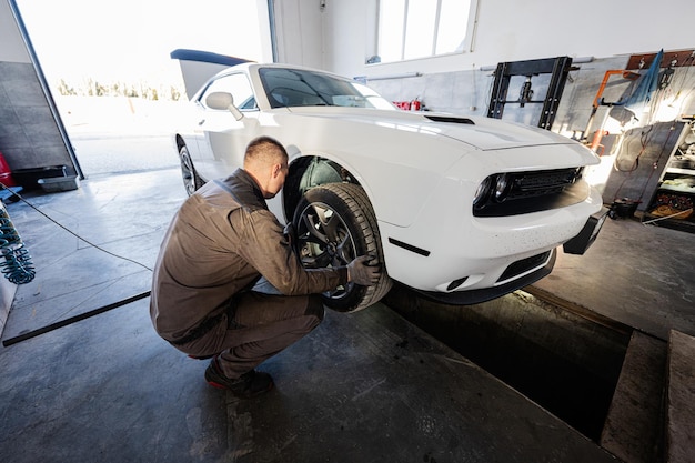 Mechanic in service repair station working with muscle car Inspects the running part of the wheel