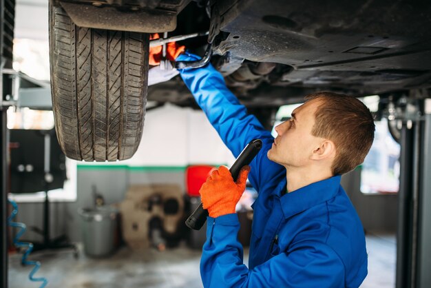 Photo mechanic with lamp checks the car suspension, repair station.