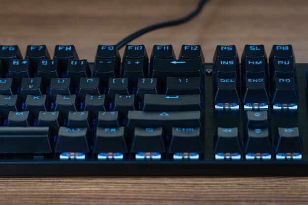 Mechanical black keyboard with blue backlight on a wooden table, close-up