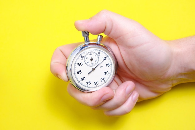 Mechanical stopwatch in a man's hand on a yellow background.