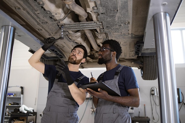 Photo mechanics inspecting car undercarriage in workshop garage