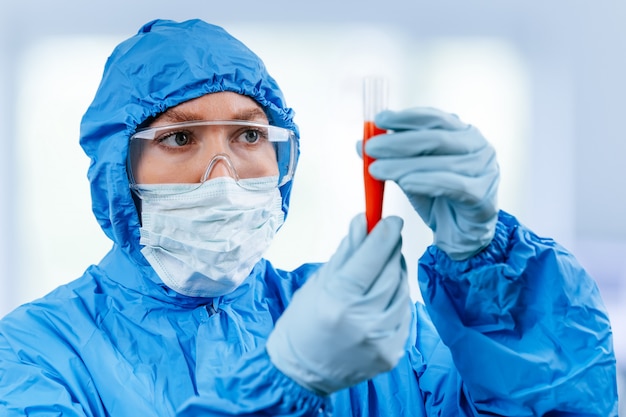 Medic in hazmat protective suit holds a test tube with a coronavirus positive blood sample from Wuhan, China. 2019 nCoV pandemic. stop coronavirus. MERS.