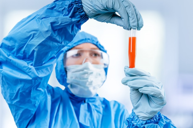 Medic in hazmat protective suit holds a test tube with a coronavirus positive blood sample from Wuhan, China. 2019 nCoV pandemic. stop coronavirus. MERS.