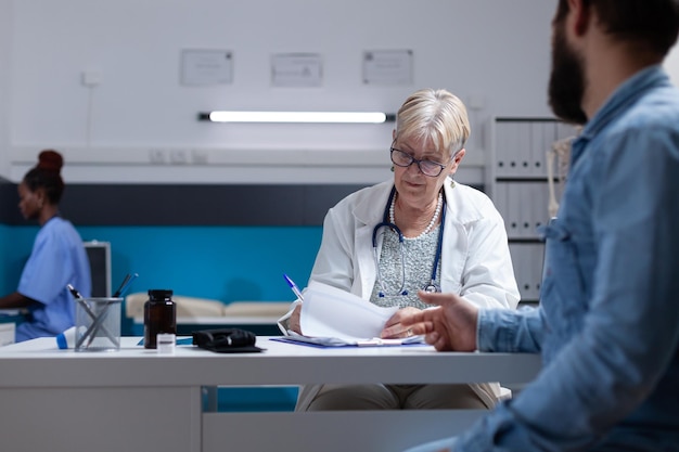 Medic signing checkup papers to give treatment to patient after examination. Physician writing prescription medicine and signature on documents to help man at medical appointment.