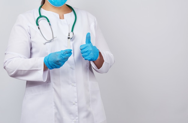 Medic woman in white coat and blue latex gloves holds a syringe and shows like gesture