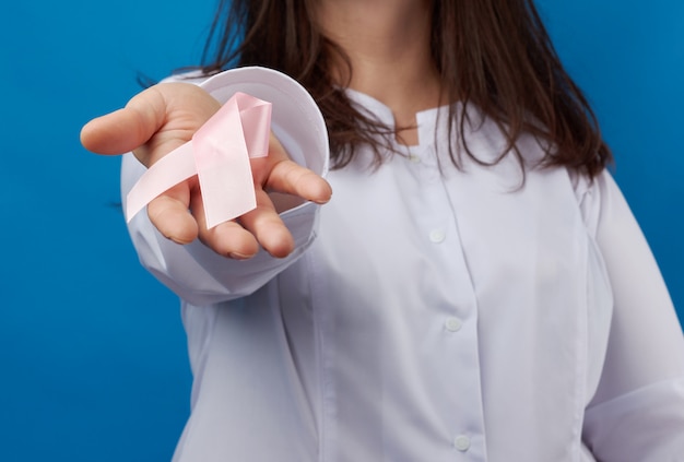 Medic woman in white coat holding silk pink ribbon in loop shape