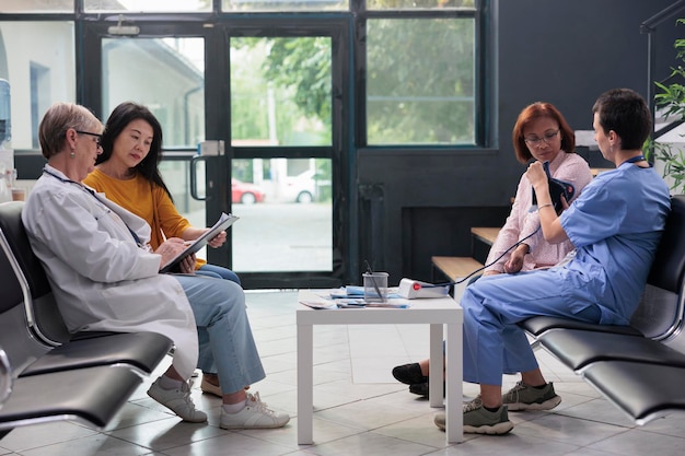 Medical assistant using tonometer instrument to measure pulse pressure and hypertension, doing cardiology examination and cardiac test in hospital lobby. Nurse and patient attending checkup visit.