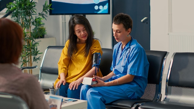 Medical assistant using tonometer to measure pulse pressure and hypertension, doing cardiology examination and cardiac test. Specialist and asian patient attending checkup visit.