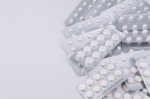 Medical blisters with pills of different sizes are stacked on the right side, isolated on a white and gray background, and copyspace on the left.