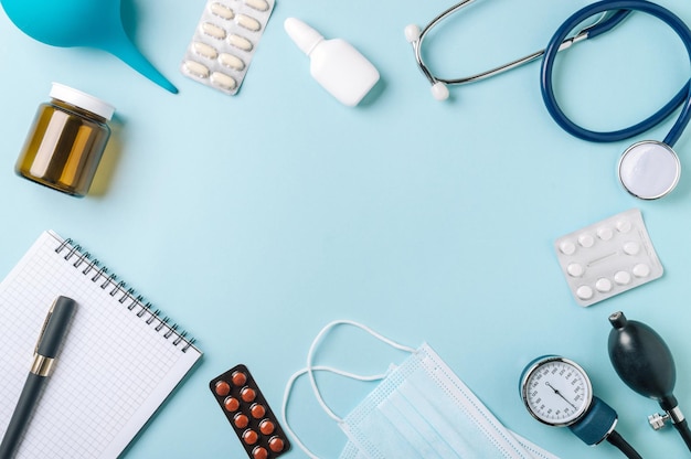 Medical concept, flat lay on blue background. Copy space in center. Stethoscope, tonometr, pills and other medical equipment on blue, top view