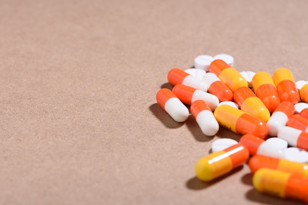 Medical concept: white, orange pills and capsules on brown background. 