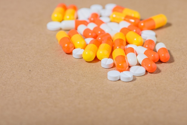 Medical concept: white, orange pills and capsules on brown background. 