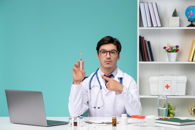 Medical cute handsome doctor in lab coat working remotely on computer holding injection