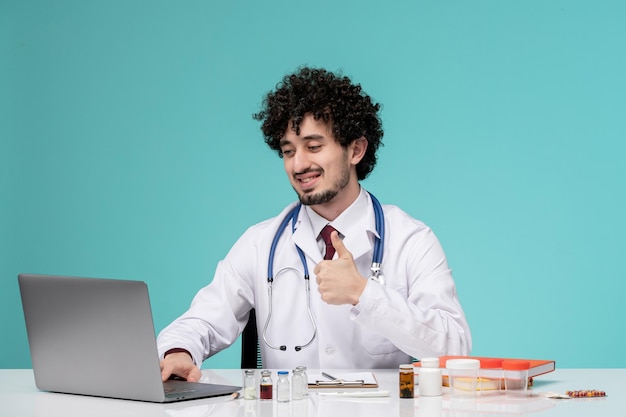 Medical cute handsome doctor working on computer remotely in lab coat showing ok gesture