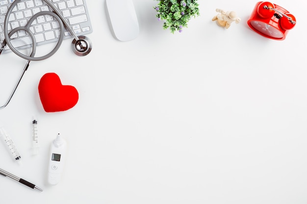 Medical desk with stethoscope,digital thermometer,heart,pen,laptop and mouse on white desk