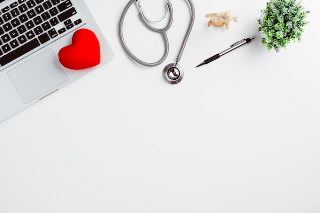 Medical desk with stethoscope,digital thermometer,heart,pen and laptop on white desk.Top v