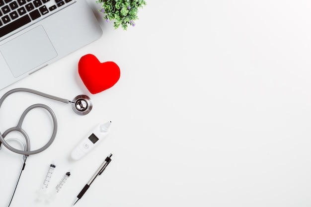 Medical desk with stethoscope,digital thermometer,heart,pen and laptop on white desk.Top v