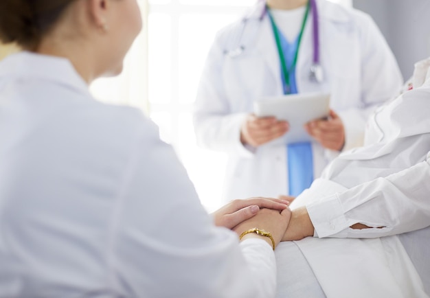 Medical doctor holing senior patient's hands and comforting her