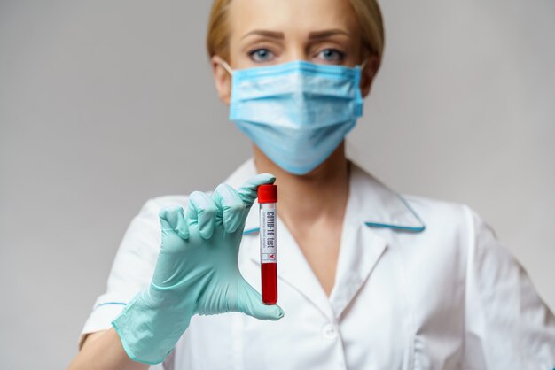 Medical doctor nurse woman wearing protective mask and gloves - holding virus blood test