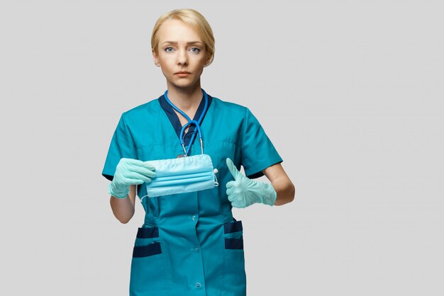 Medical doctor nurse woman with stethoscope over light grey wall - showing protective mask