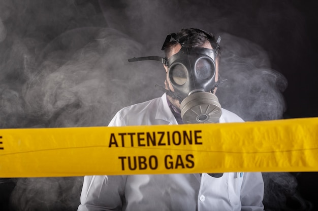 A medical engineer wearing antigas mask experienced in the gas leaks crisis directing the emergency during the chaos. On the yellow tape the written notice "attention gas tube"