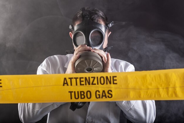 A medical engineer wearing antigas mask experienced in the gas leaks crisis directing the emergency during the chaos. On the yellow tape the written notice "attention gas tube"