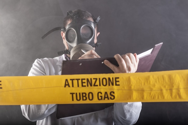 A medical engineer wearing antigas mask experienced in the gas leaks crisis directing the emergency during the chaos. On the yellow tape the written notice "attention gas tube"