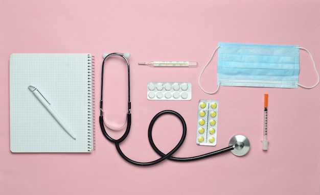 Medical equipment on a pink pastel background. Blisters pills, notepad, stethoscope, thermometer, manometer. Medical concept, top view, flat lay style