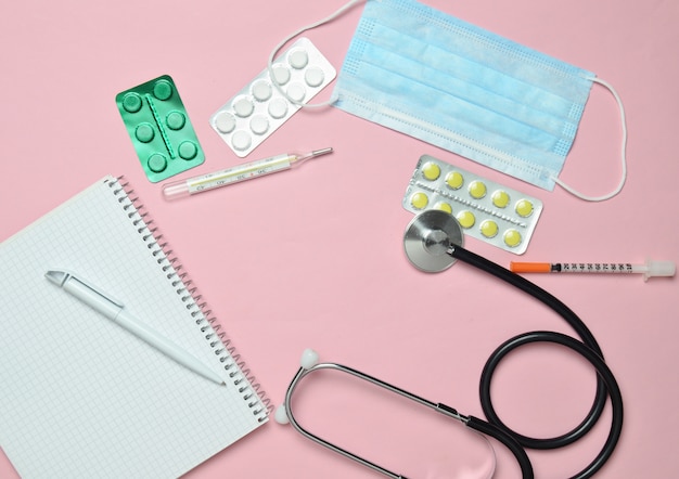 Medical equipment on a pink pastel background. Blisters pills, notepad, stethoscope, thermometer. Medical concept, top view, flat lay style