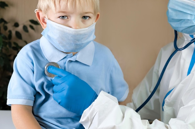 Medical examining boy in clinic Little child checked by doctor Pediatrician with stethoscope with face mask and toddler in a hospital Check heart lungs of kid Pediatric checkup in hospital