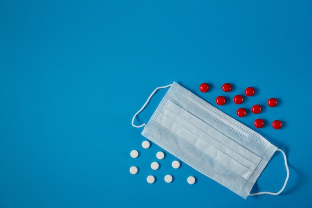 Medical face mask and pills on blue background