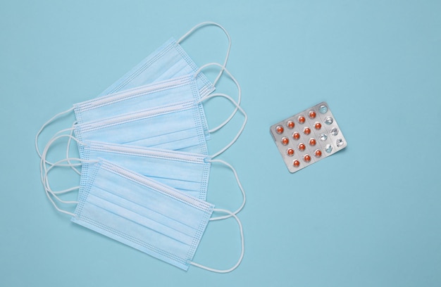 Medical facial masks and blister of pills on a blue background Top view