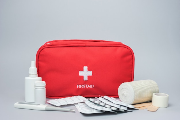 Medical first aid kit with medicine and pills. Isolated on gray background. Red bag with medical equipment and medications for emergency.