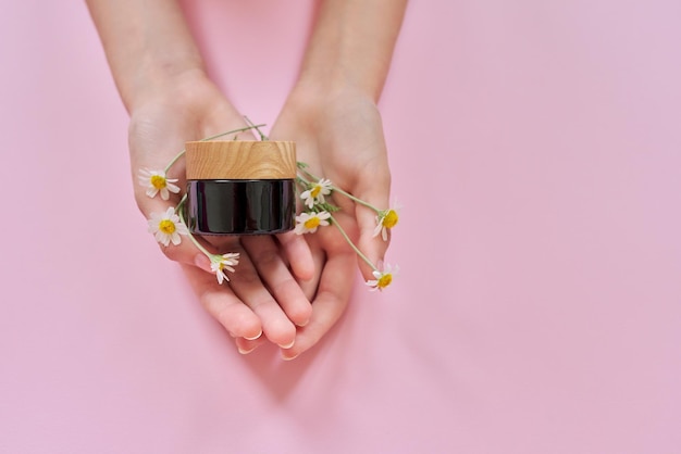 Medical herbal natural cosmetics with chamomile Woman hands flowers and glass bottle with product on pink background top view