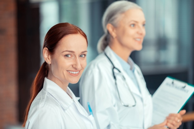 Medical insurance. Beautiful smiling red-haired young female doctor in a white coat standing next to her colleague