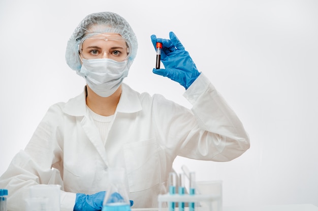 Medical laboratory assistant in a mask on a white background, holds a test tube with the blood of an infected person.