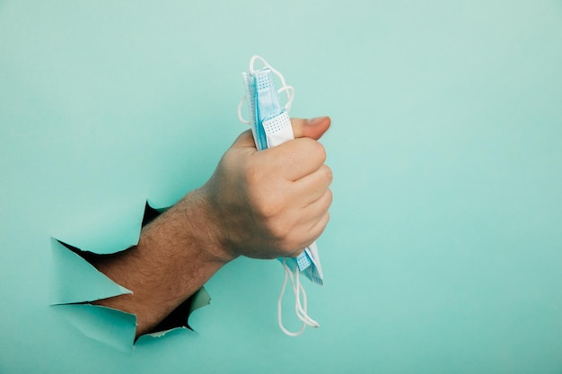 Medical mask in a male hand on a blue background with a hole medical concept