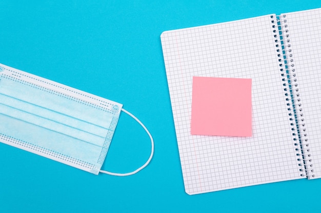 A medical mask and a note pad lying on blue table