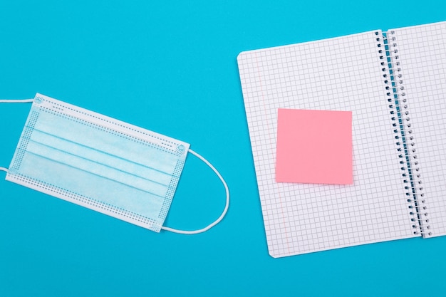 A medical mask and a note pad lying on blue table