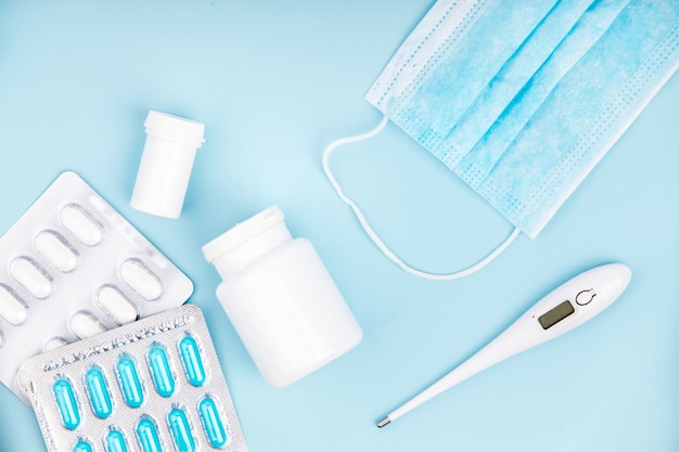 Medical mask, pills and thermometer on blue background