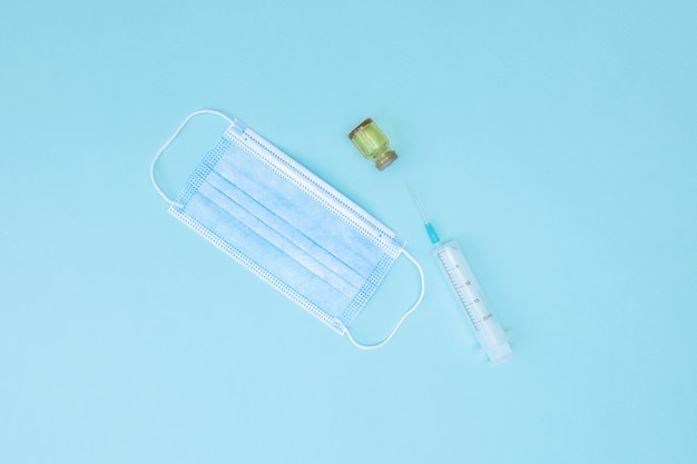 Medical mask, syringe and jar. A disposable surgical face mask covers the mouth and nose. Healthcare and medical concept.