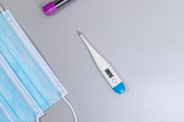 Medical mask and thermometer on gray table