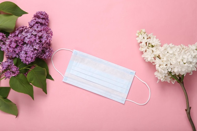 Medical mask with flowering branches of lilac on pink background